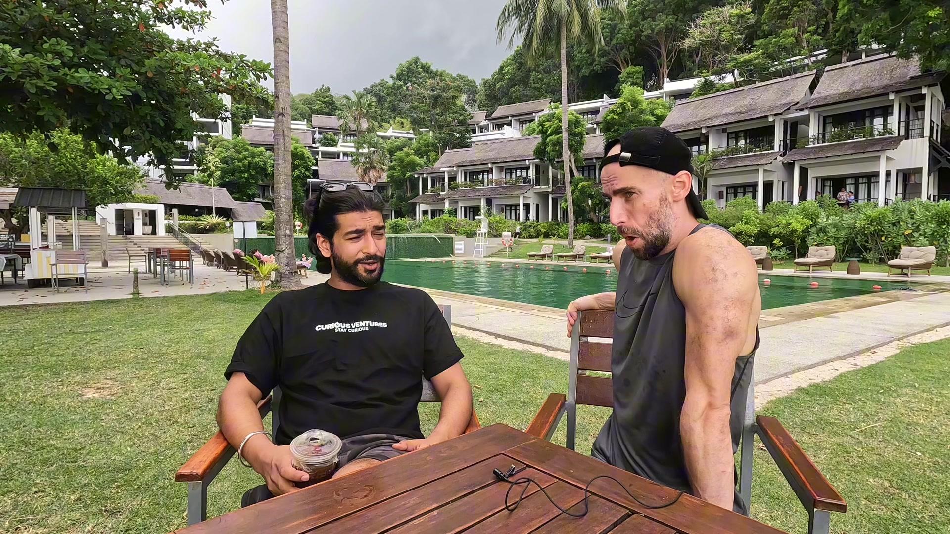 Ashish Sood, in a Curious Ventures 'stay curious' shirt, and Konrad talking by a resort pool at Network School